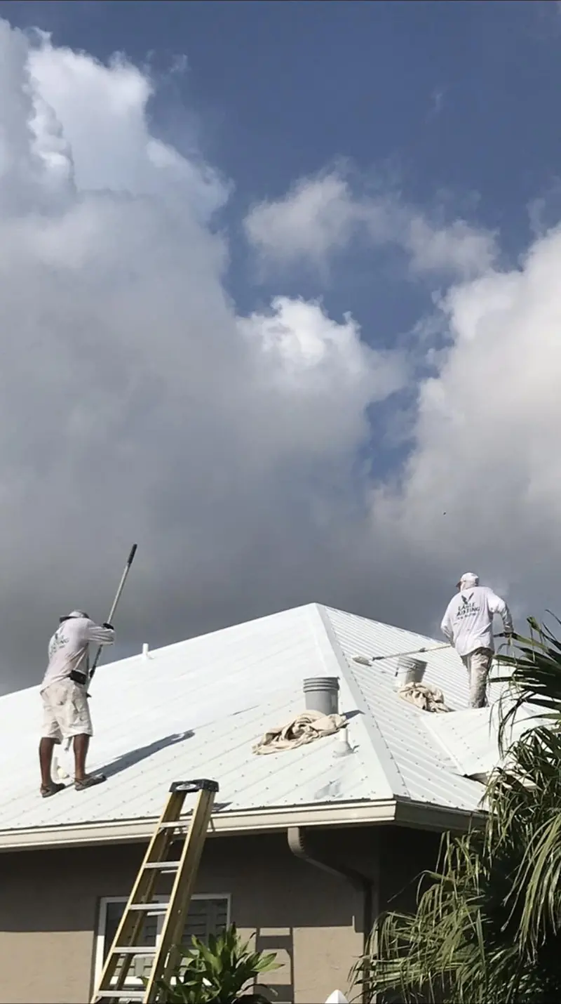 Painters on ladders finishing a white roofline and fascia on a Florida home
